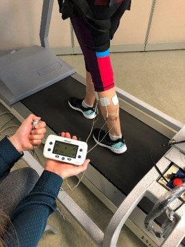 person with electronic device connected to their leg with leads walking on a treadmill
